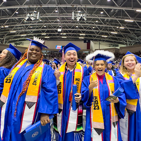A group of inaugural graduates of the education bachelor's degree stand in their caps and gowns