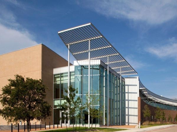 The image is of the M building on the Cedar Valley Campus. This building has courses for the veterinary technology degree program and courses for life sciences programs.  The building is tall, having two floors, and is one of the newest buildings on the campus, with lots of grass, trees and plants. It is a green building, with more efficient electricity usage, more windows for natural light, and more accessible entry ways.