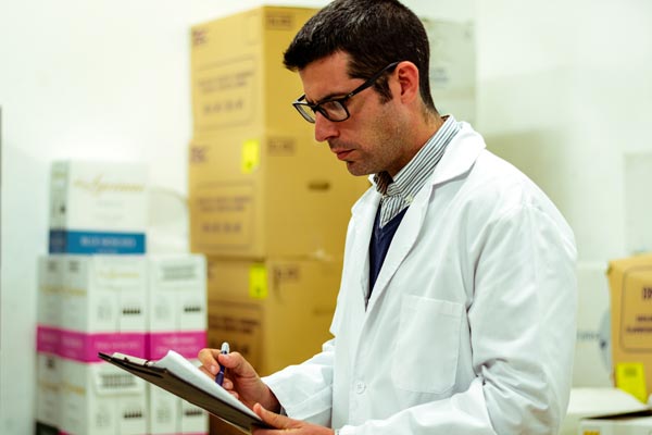 Man wearing labcoat with clipboard and boxes