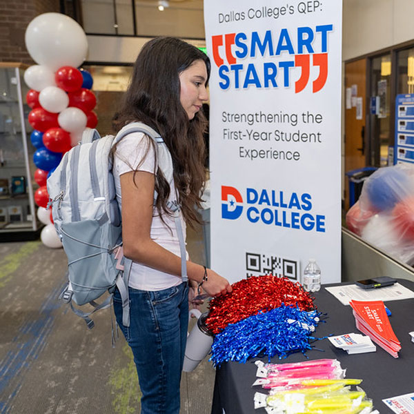 Student at a Dallas College Smart Start table with pom-poms, glow sticks, and an informational banner.