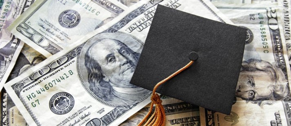 A graduation cap rests atop a pile of cash