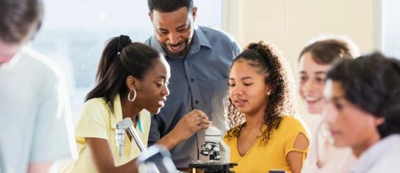 A teacher shows young students how to use a microscope