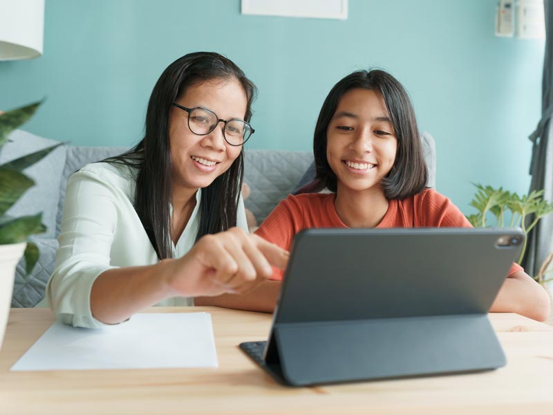 Mother and daughter at a table looking at a tablet, mother pointing at the screen.