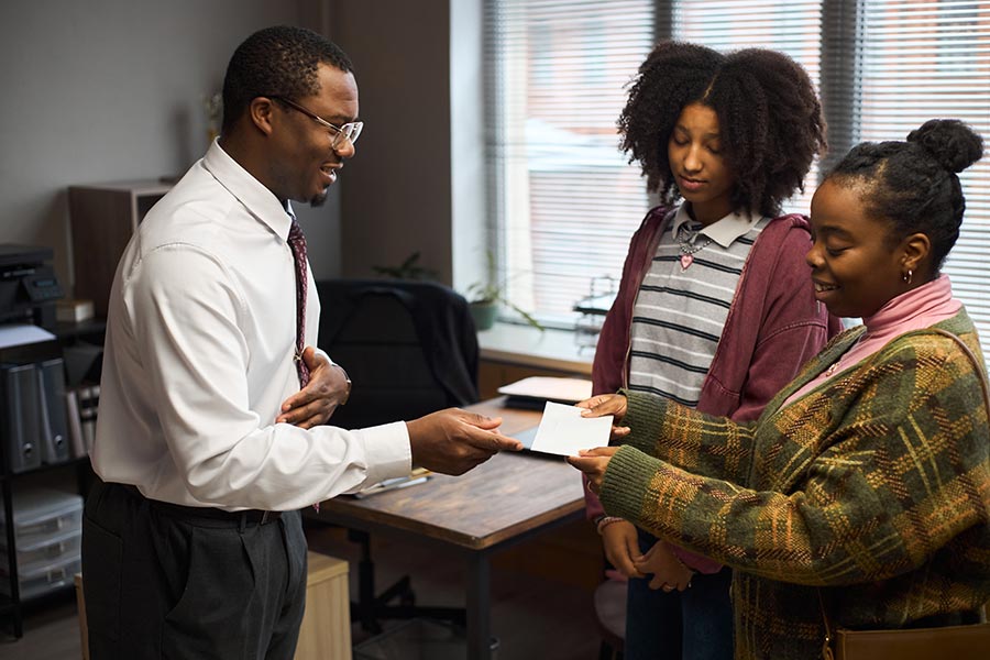 Middle Aged Black Man Acting as School Principal Greeting Two Teen Girls
