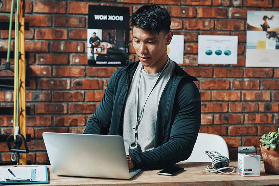 male fitness teacher sitting at laptop wearing athletic clothing