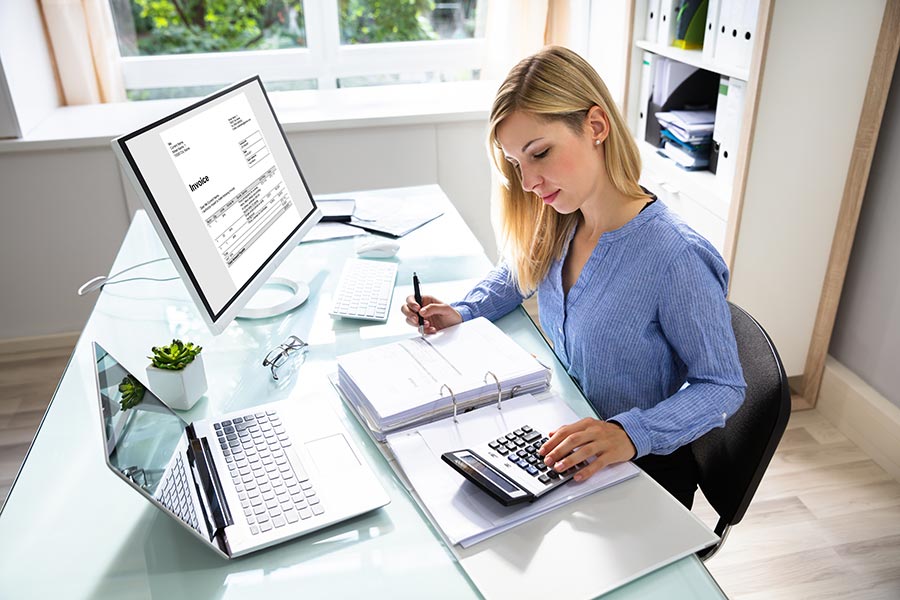 A woman sitting at a desk working with a calculator and laptop.