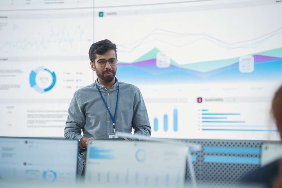 male worker standing in front of a large screen with graphs and charts