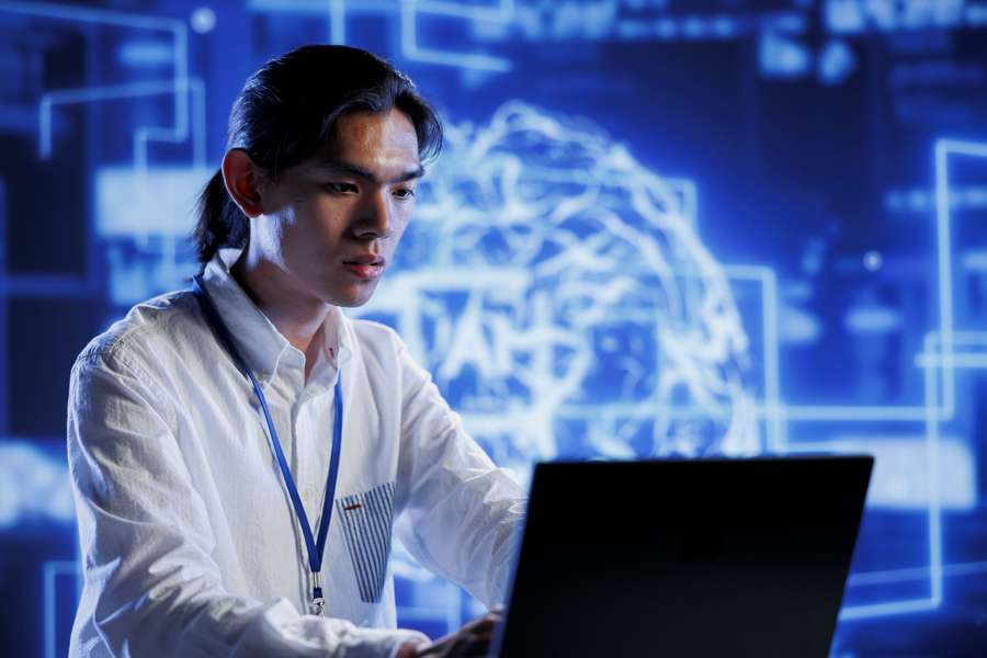 male workers in a white collared shirt sitting in front of a laptop with a blue backdrop