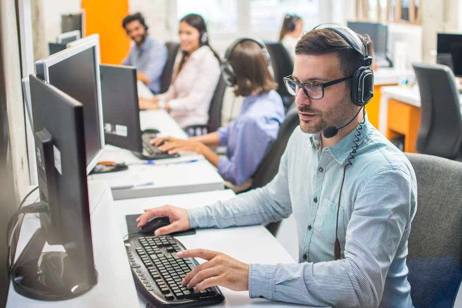male worker sitting at a long computer desk with other workers