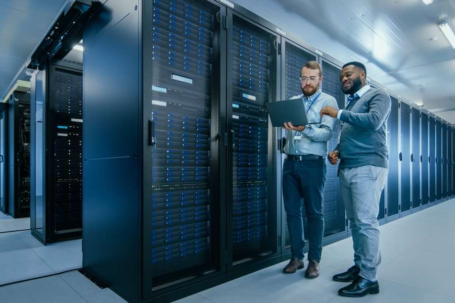 two male coworkers standing in a hallway looking at a laptop together