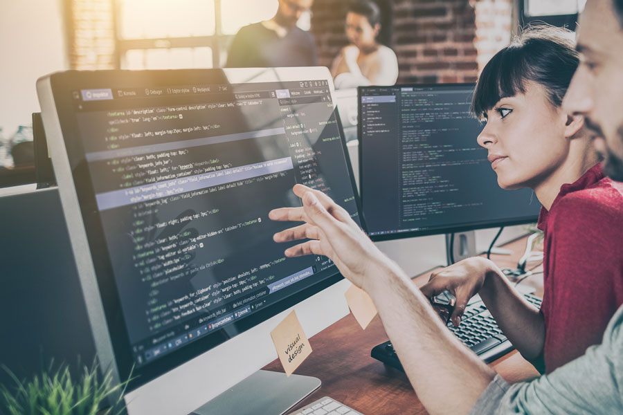 man and woman sitting side by side looking at a computer monitor with coding language displayed