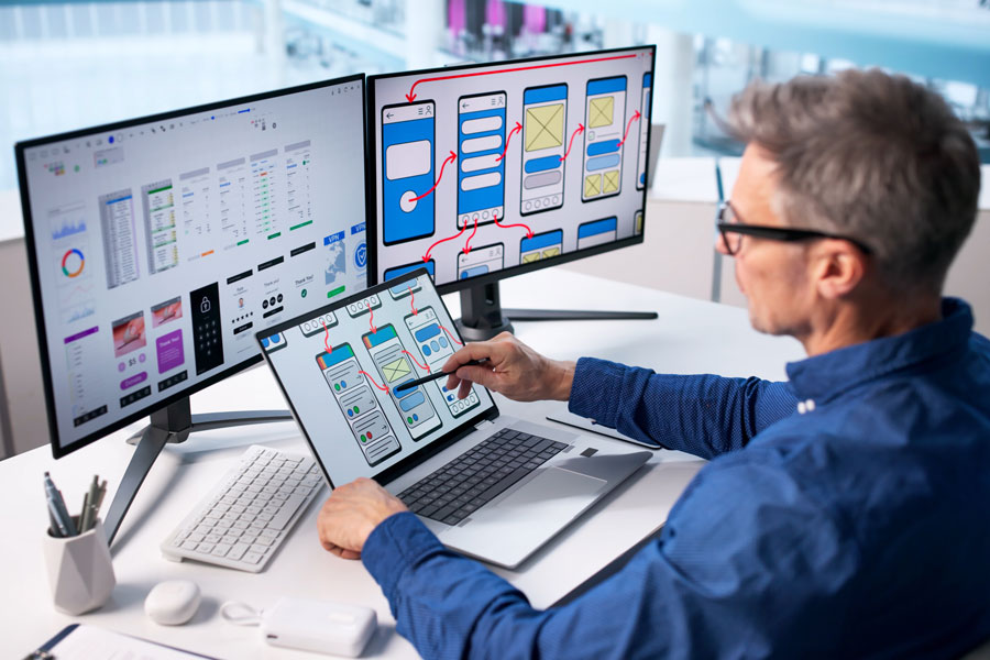 Businessman Creating User-friendly Website on a laptop with monitors at a desk