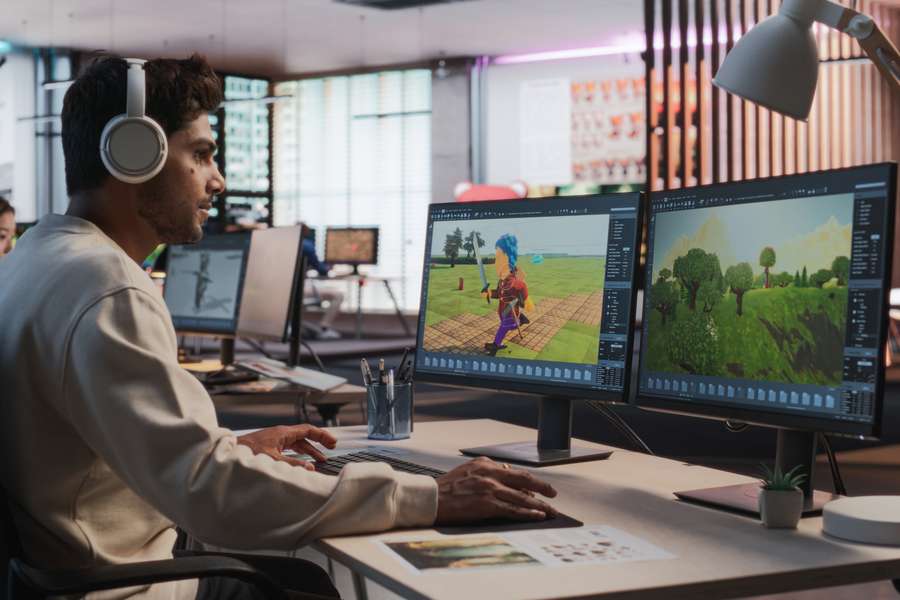 male sitting at a computer desk with two monitors playing and designing a game
