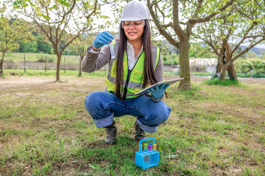 female in uniform and hard hat kneeling down in a lawn with a test tube