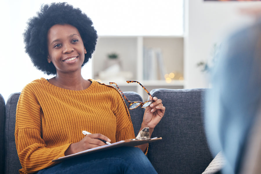 Female psychologist in orange shirt on couch writing notes with patient.