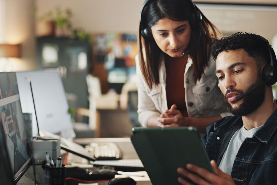 male and female coworkers with headphones on and looking at a tablet together