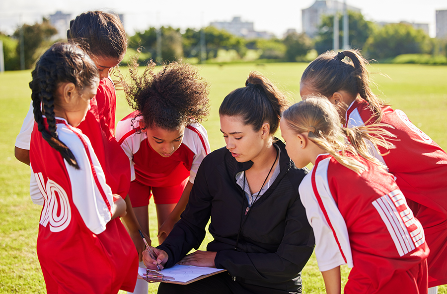 female coach surrounded by girls soccer team wearing red jerseys