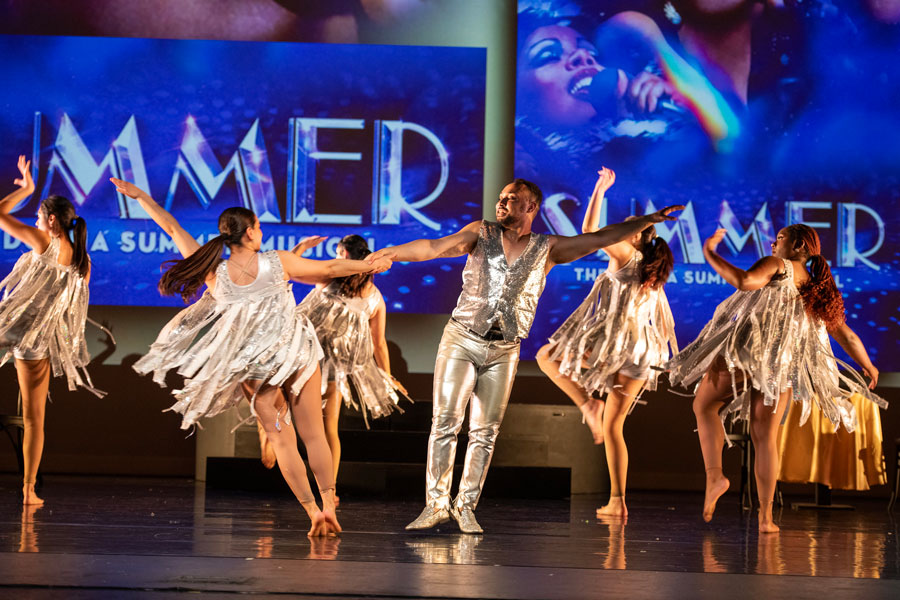 a group of male and female dancers on stage in silver costumes