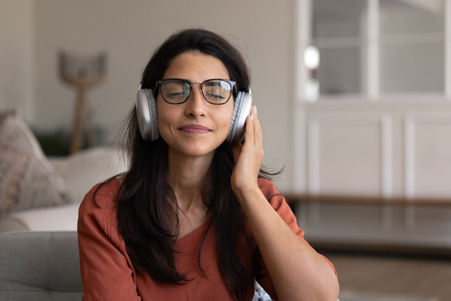 Positive peaceful Hispanic woman in headphones relaxing at home