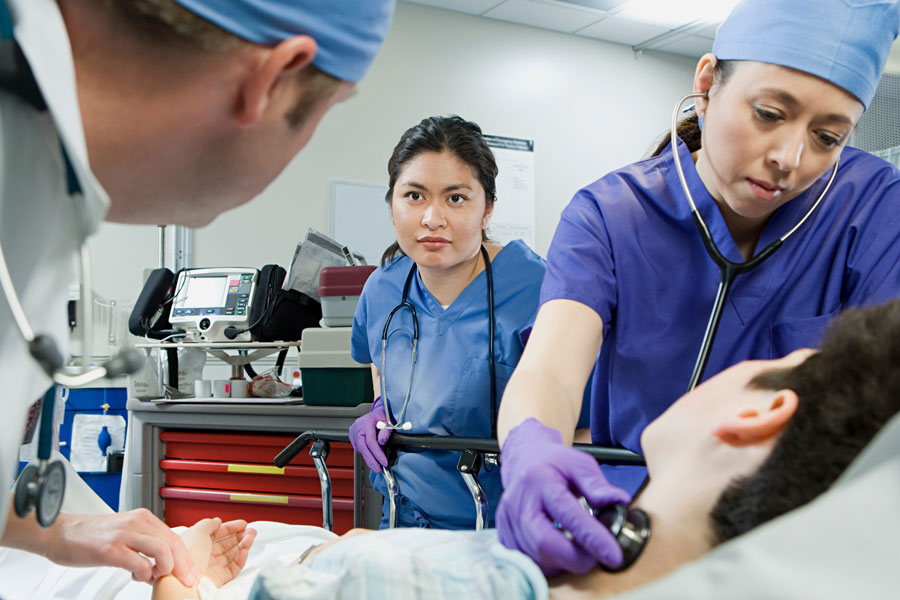 two female nurses and one male doctor examining a male patient lying on a stretcher