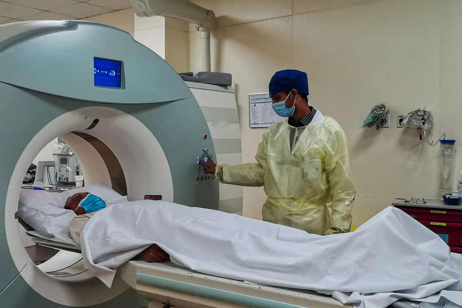 Computed Tomography machine (CT) in Radiology Department with radiology technician wearing personal protective equipment preparing patient for examination