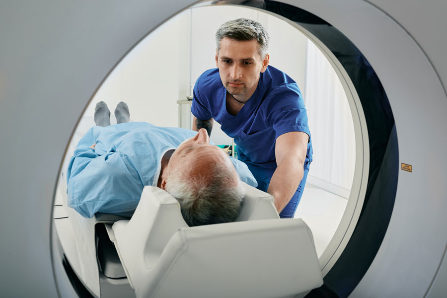 Senior man going into CT scanner. CT scan technologist overlooking patient in Computed Tomography scanner during preparation for procedure