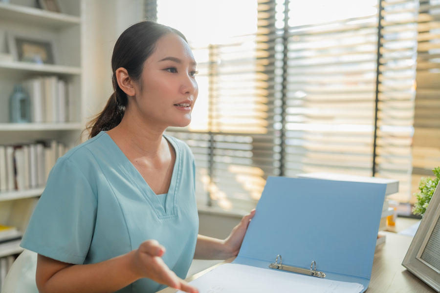 Female healthcare professional reviewing medical documents at desk with laptop in clinic office