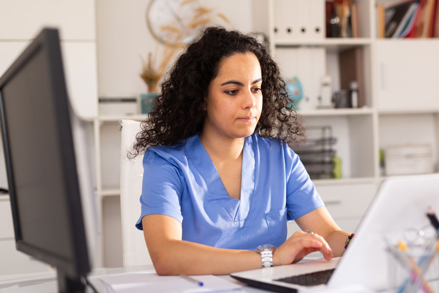 Female health tech in blue top working on laptop in office