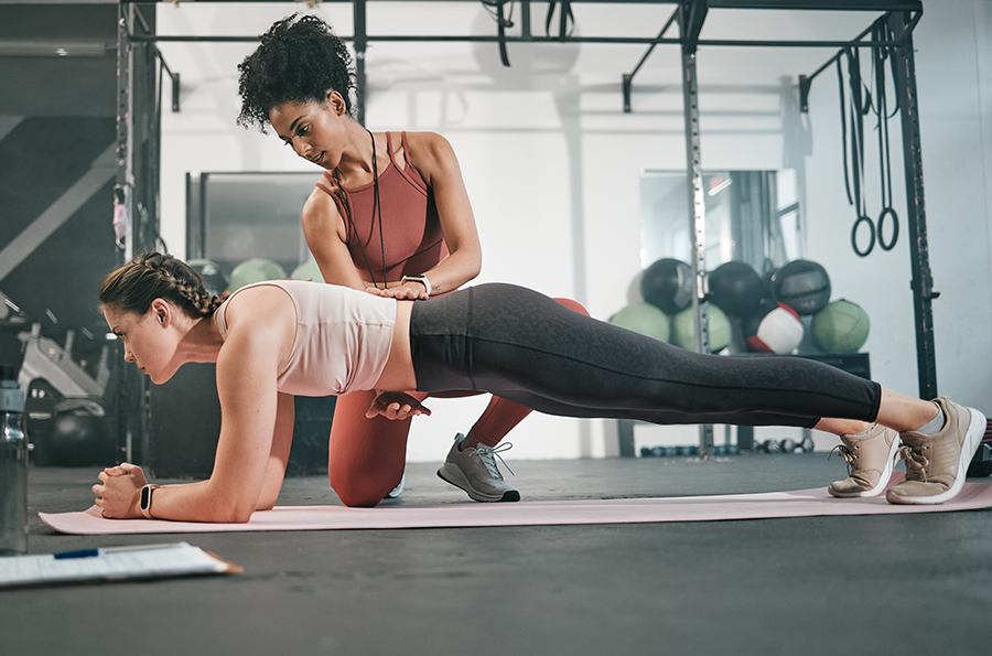 female athletic trainer working with female client who is doing a plank in a gym