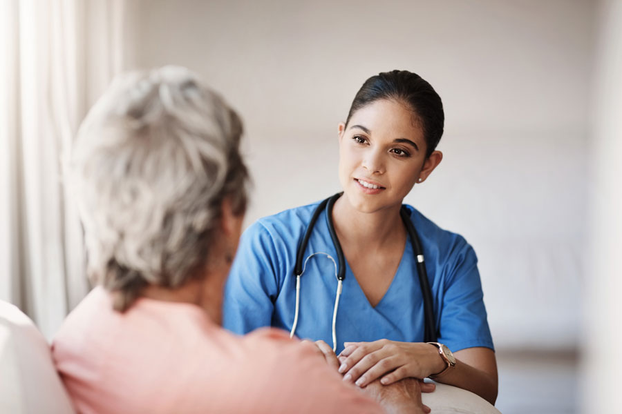 Female nurse with a senior female patient sitting and chatting together.