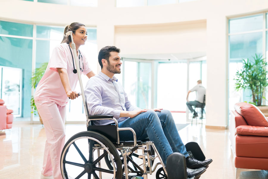 Female Healthcare Worker Wheeling Adult Male Patient In Hospital