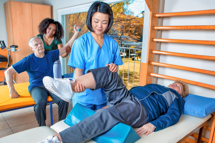 female occupational therapist helping an elderly lady stretch her leg on a table