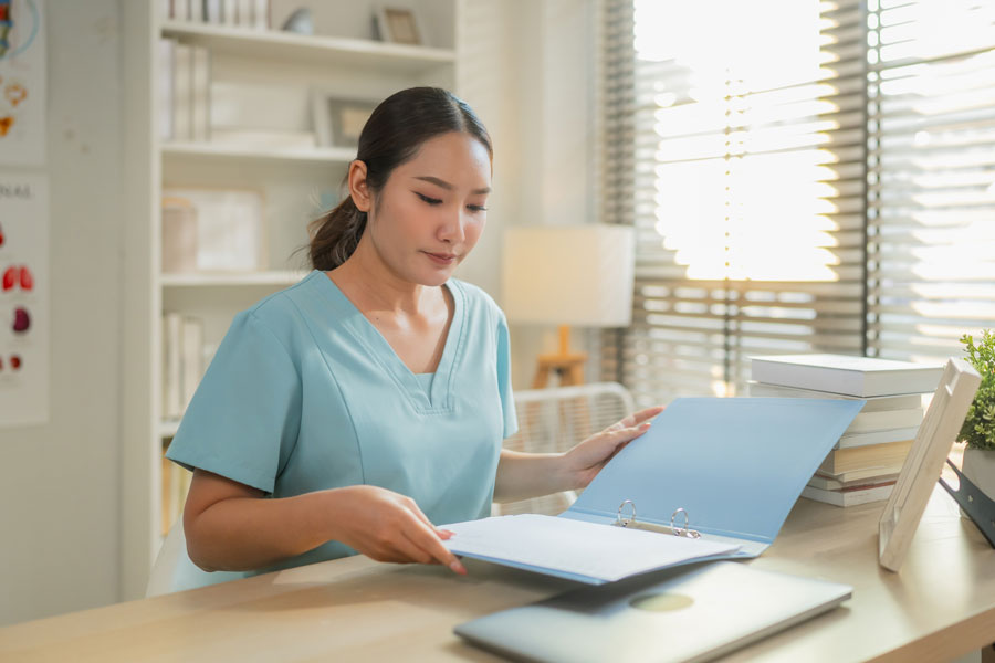 Female healthcare professional reviewing medical documents at desk with laptop in clinic office