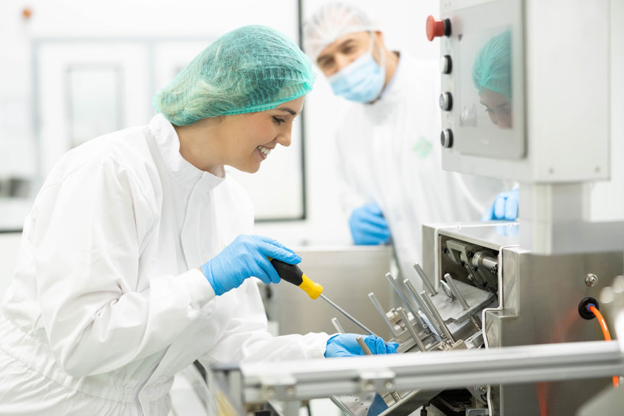 A woman wearing a hairnet inspects high-tech medical equipment in a clean room