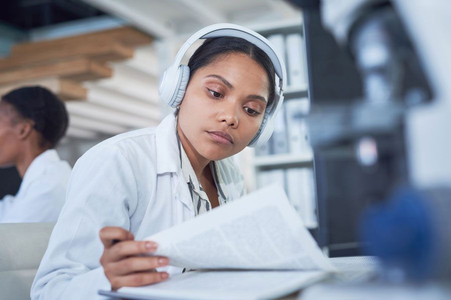 Woman in a white shirt sitting at a desk wearing white headphones and reading papers