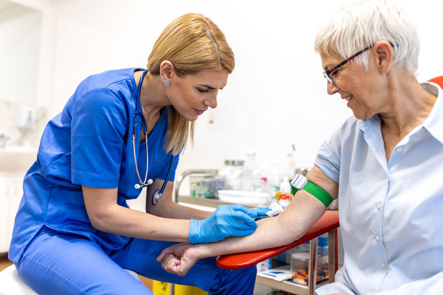 Female nurse in blue scrubs taking a blood sample from the arm of a senior female patient
