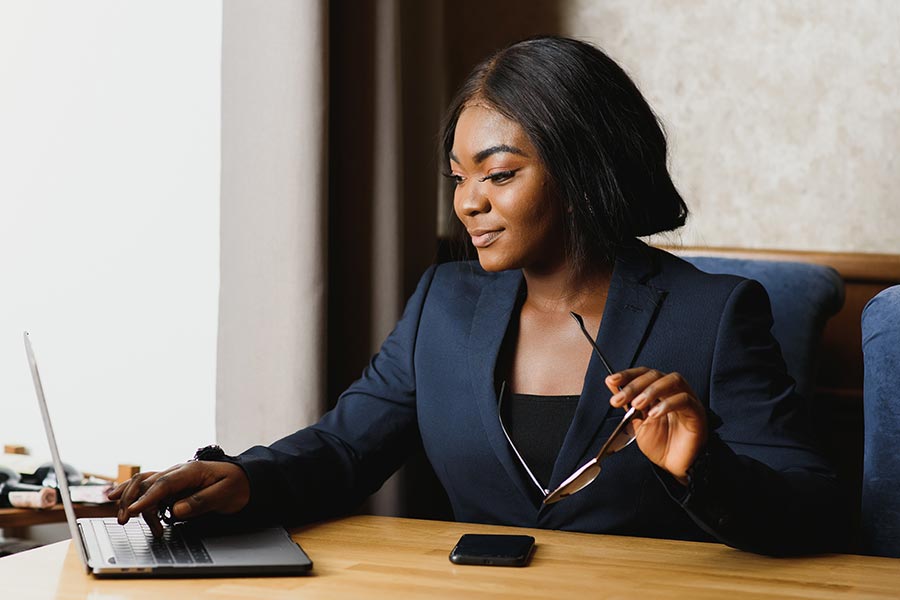 Business professional working on a laptop at a desk while holding a pair of eyeglasses, with a smartphone resting beside the computer.