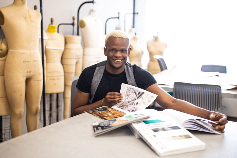 male fashion student sitting at a table flipping through fashion magazines