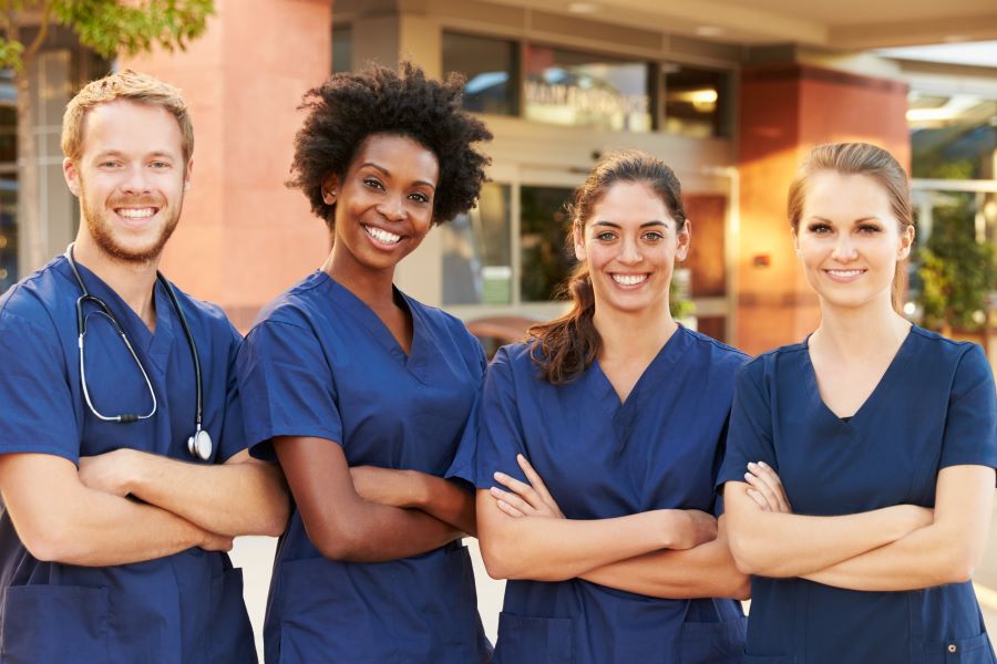 A group of nurses stand outside a hospital with their arms folded
