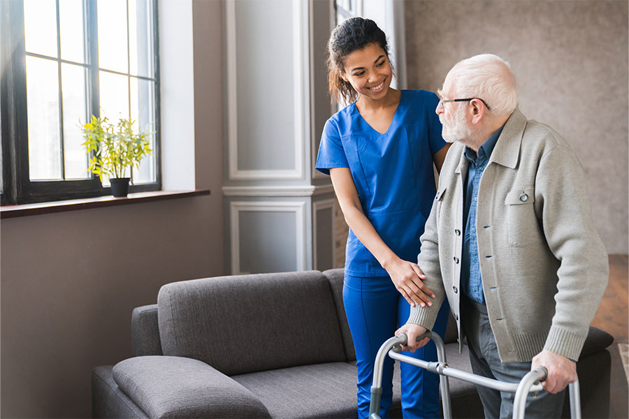 Nurse assisting elderly man with walker.