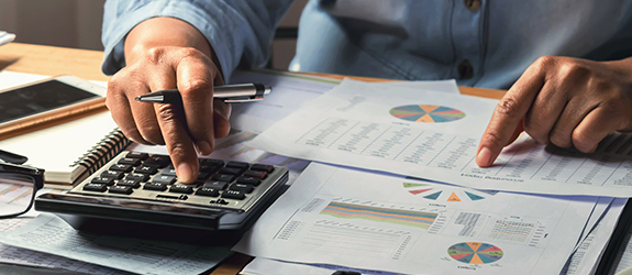 A person reviews charts on their desk while using a calculator