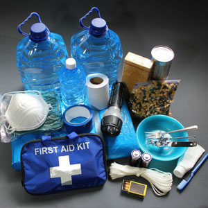 Emergency preparedness kit with two large water jugs, a first aid kit, flashlight, canned food, face mask, and basic utensils