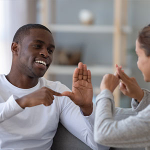 Smiling man and woman communicating using sign language in a cozy living room, conveying warmth and connection