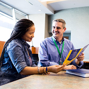 A man in a blue shirt showing a brochure to a woman at a table