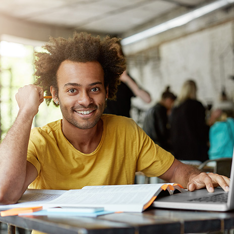 Student works with a laptop and an open book at a desk