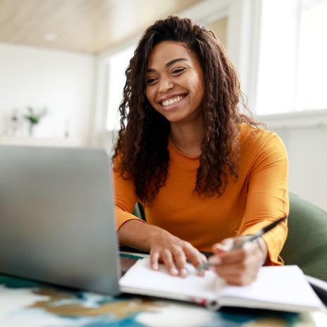 Student writes in her notebook while looking at her laptop screen