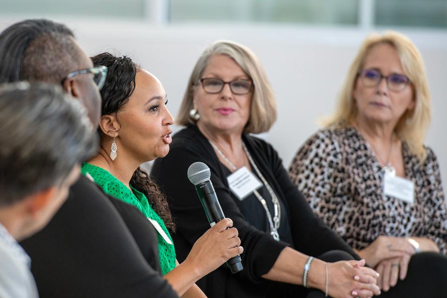 Panel discussion at Business Technology Symposium 2024 with five professionals engaged in conversation, one holding a microphone.