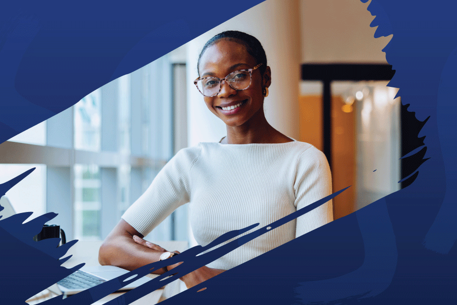 a smiling woman sits at a table with a laptop and coffee mug on it