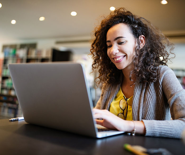 Student with curly hair using a laptop at a table in a library-like setting