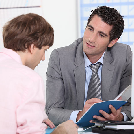 A Dual Credit instructor and a student are discussing a blue folder at a table